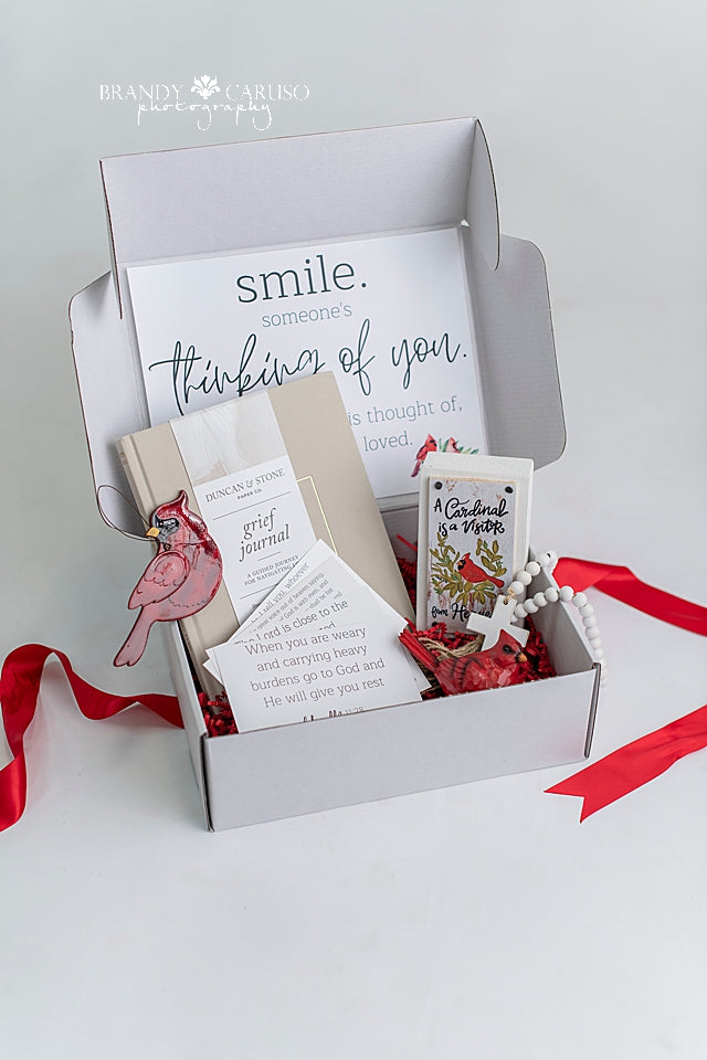 Cardinal themed sympathy gift box that includes a guided grief journal, assorted Cardinal trinkets, a cross and a Cardinal table qoute. 